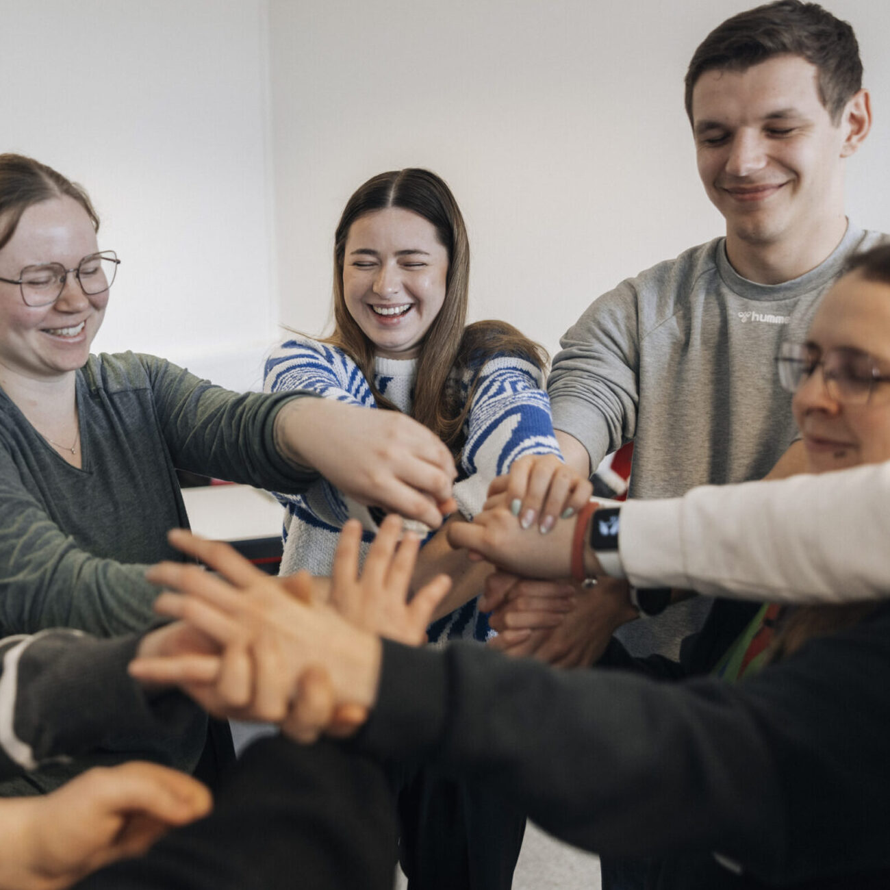Eine Gruppe von Schülerinnen und Schülern hält sich an den Händen. Dabei sind ihre Augen geschlossen.