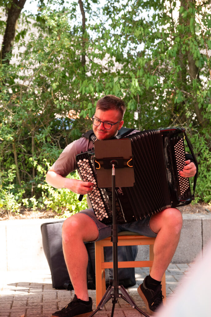 Marko Basara sitzt mit einem Akkordeon im Garten des Seniorenclubs und spielt während eines Konzerts für die Bewohner:innen des St. Josefs-Stifts.
