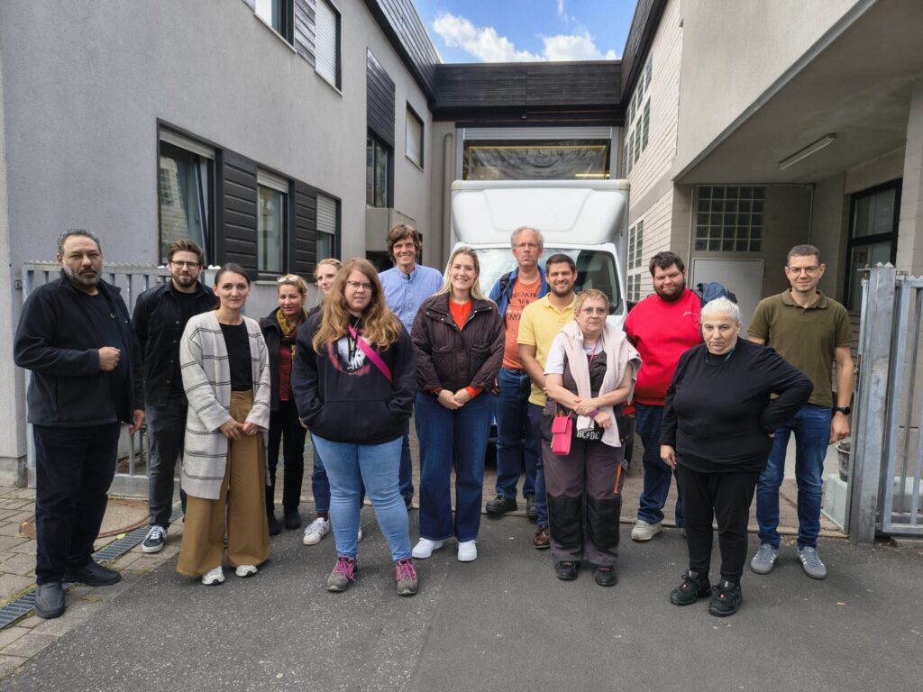 Teilnehmende von WfbM, Reciclage und Stadt Aschaffenburg stehen gemeinsam auf dem Werkstattgelände vor einem weißen Transporter.
