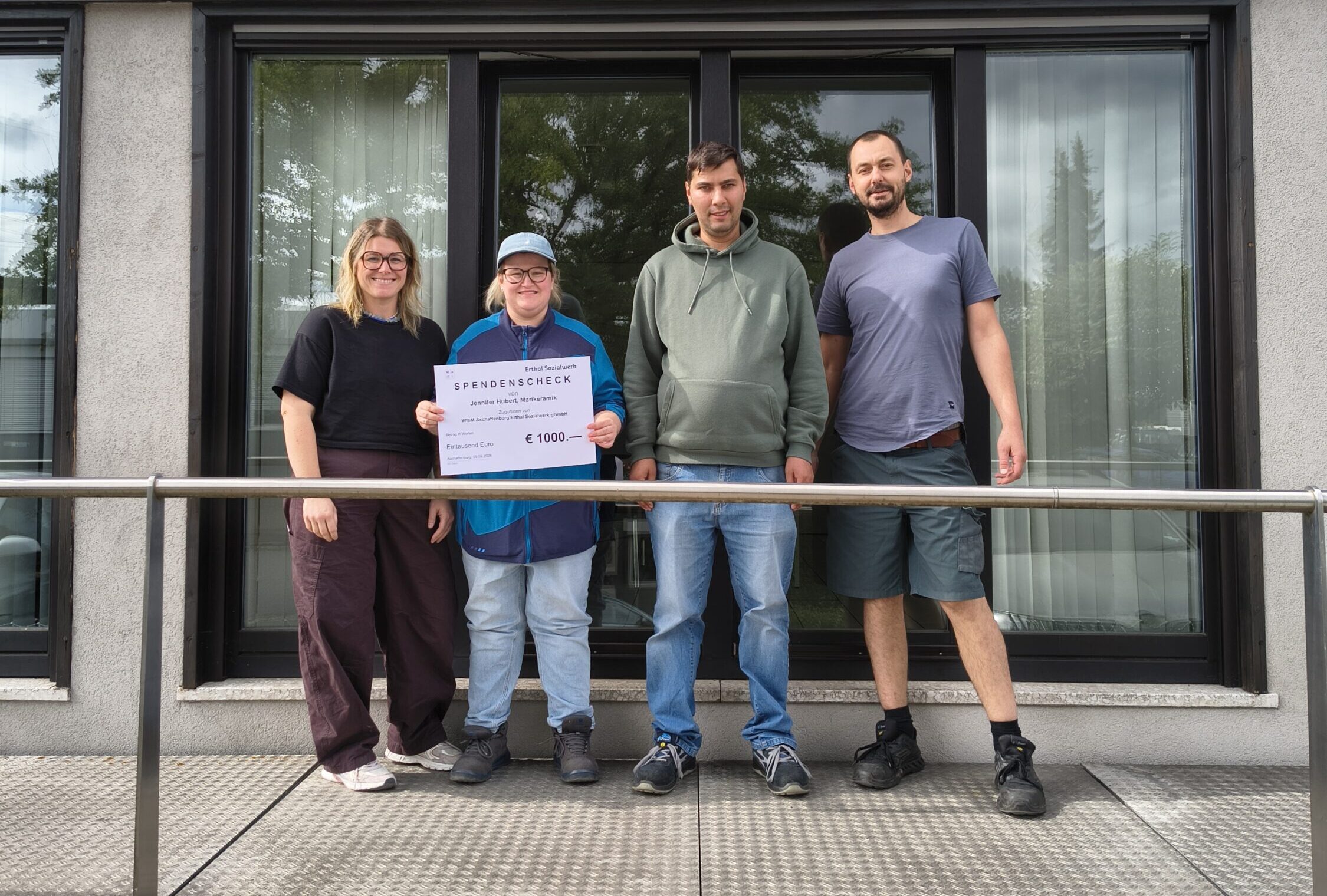 Jennifer Huber, zwei Beschäftigte der WfbM und Matthias Steinberg präsentieren einen Spendenscheck über 1.000 Euro.